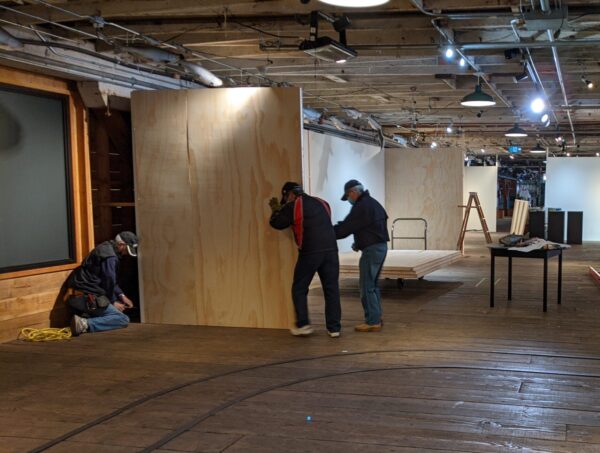 Three men installing a wooden wall inside historic cannery museum