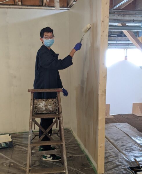 Young volunteer on ladder painting wall with white paint
