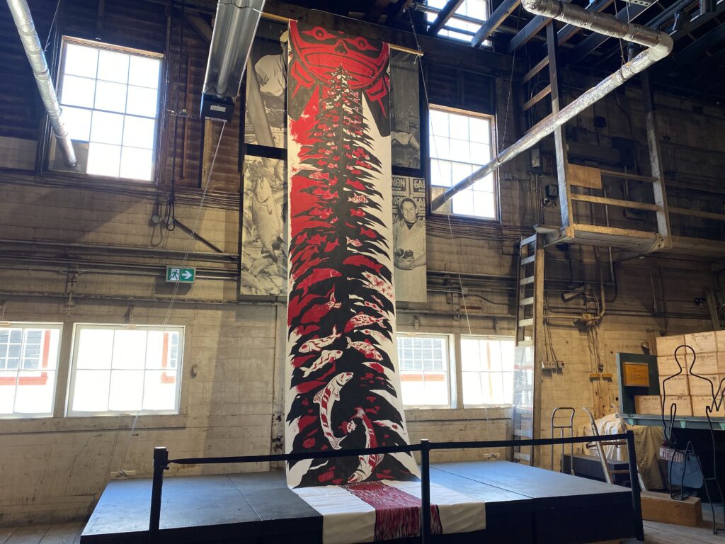 long vertical banner suspended from building rafters depicting First Nations art in black, white and red design