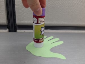 hand holding glue stick on top of hand-shaped green paper